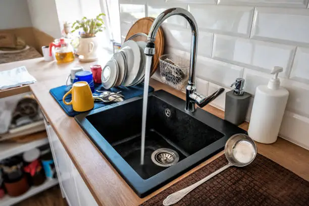 Water flowing out of a kitchen stainless steel tap into the sink. Wasting water by leaving a chrome faucet tap running